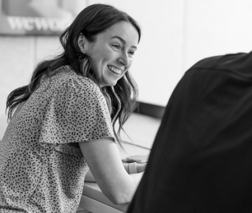 A woman sitting at a desk smiling to someone offscreen.