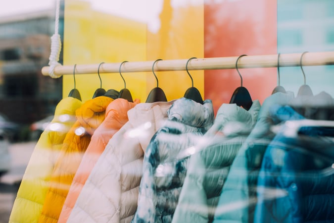Colorful jackets on coat hangers hanging from a coat rack.