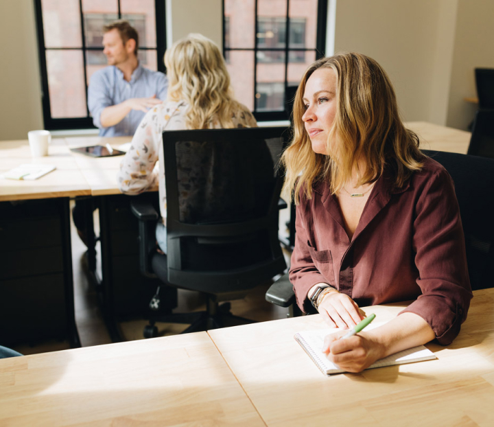 Woman sitting at a desk taking notes in a notebook.