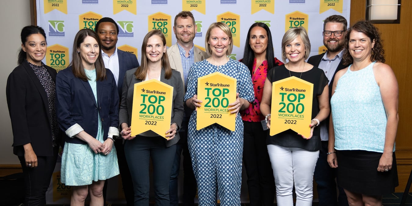 Pioneer Management Consulting team members holding Star Tribune Top 200 Workplaces signs.