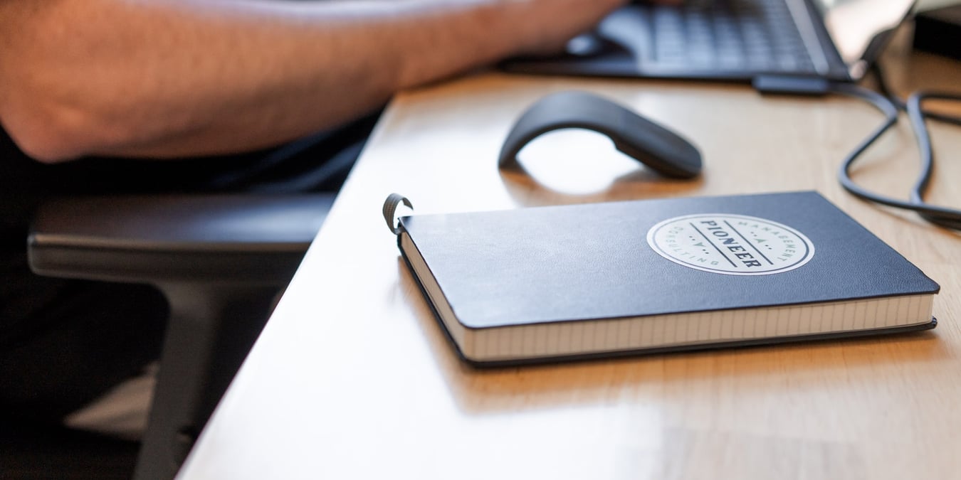 A Pioneer Management Consulting branded notebook on a desk.