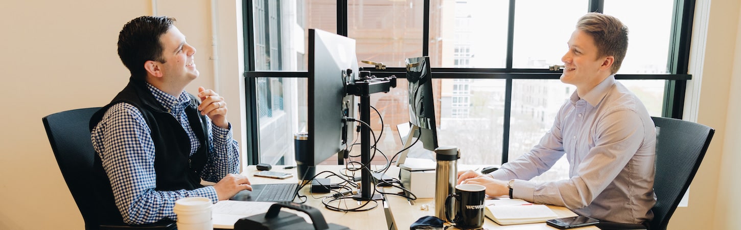 Two men sitting at computer desks across from each other.