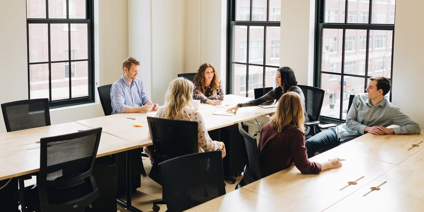 A few people sitting at tables in a bright conference room.